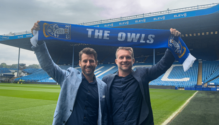 Nick and Danny from One2Call hold Owls scarf above their head in front of the stand at Hillsborough